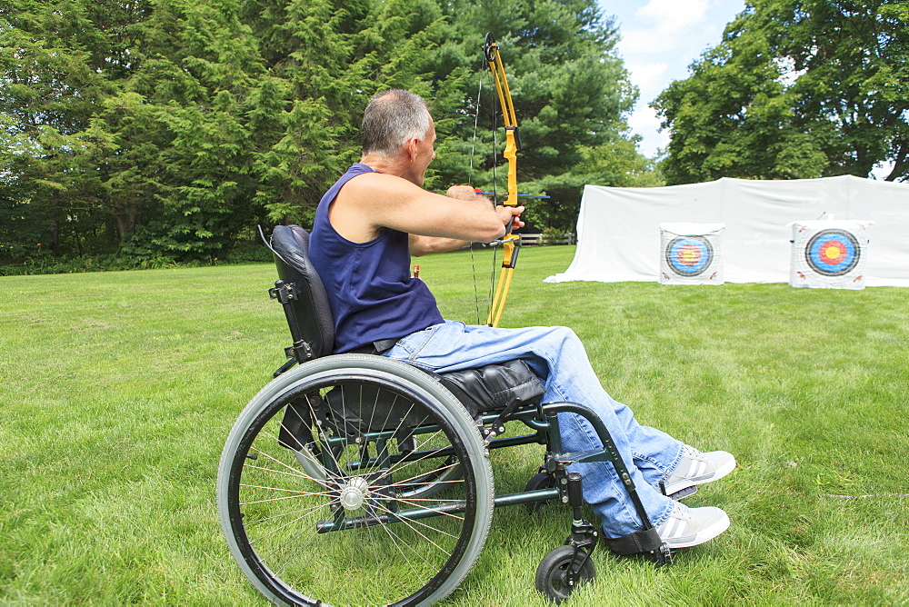 Man with spinal cord injury in wheelchair aiming his bow and arrow for archery practice