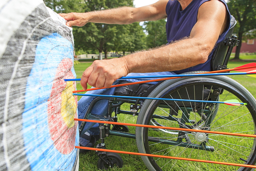 Man with spinal cord injury in wheelchair removing arrows from target after archery practice