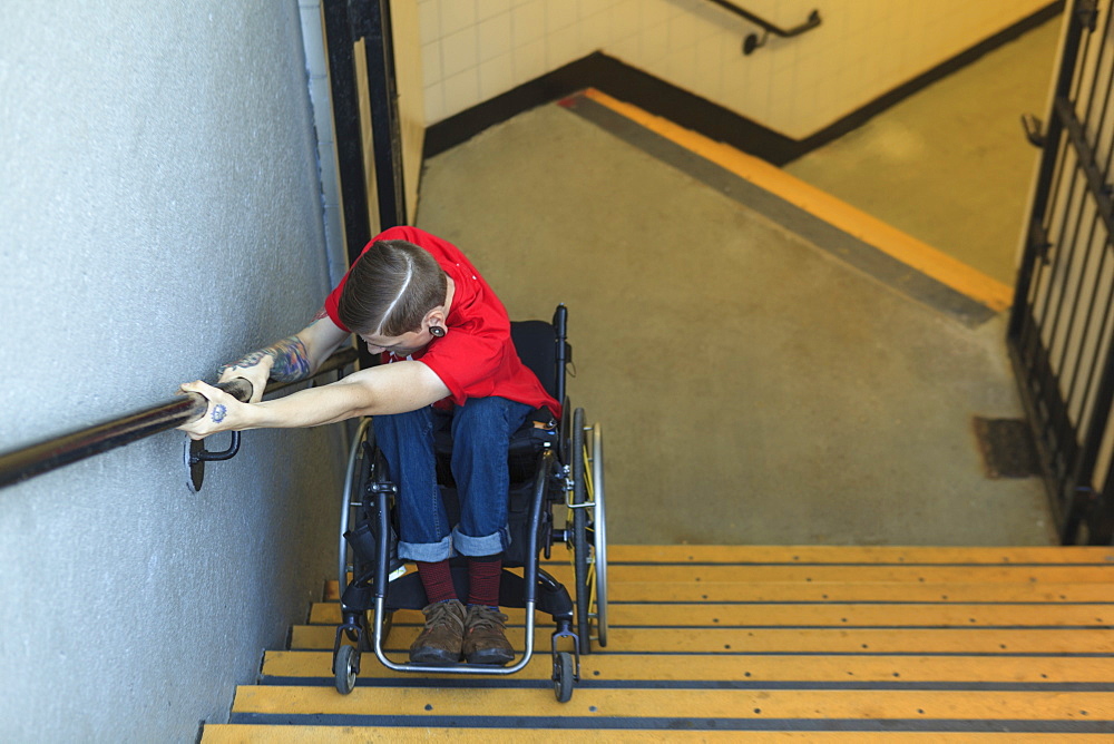 Trendy man with a spinal cord injury in wheelchair going down subway stairs backwards