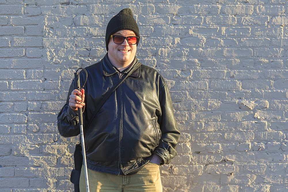 Man with congenital blindness standing in front of a wall with his cane