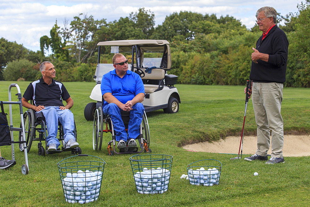 Two men in wheelchairs with spinal cord injuries learning golf from an instructor