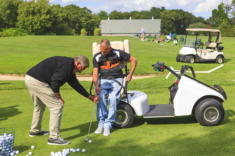 Man with spinal cord injury in an adaptive cart at golf putting green with an instructor