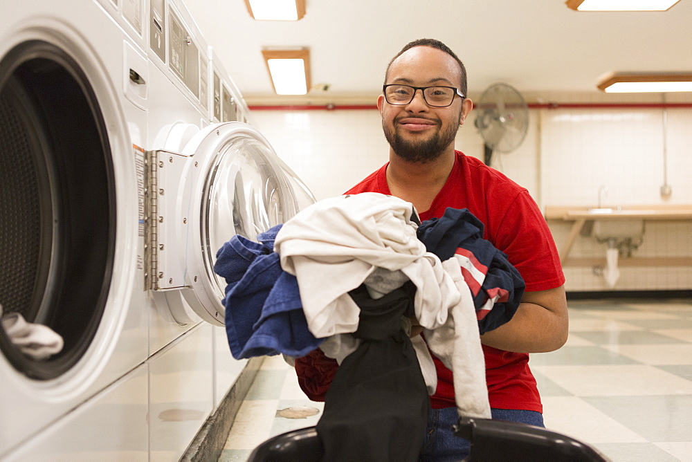 Happy African American man with Down Syndrome doing laundry in utility room