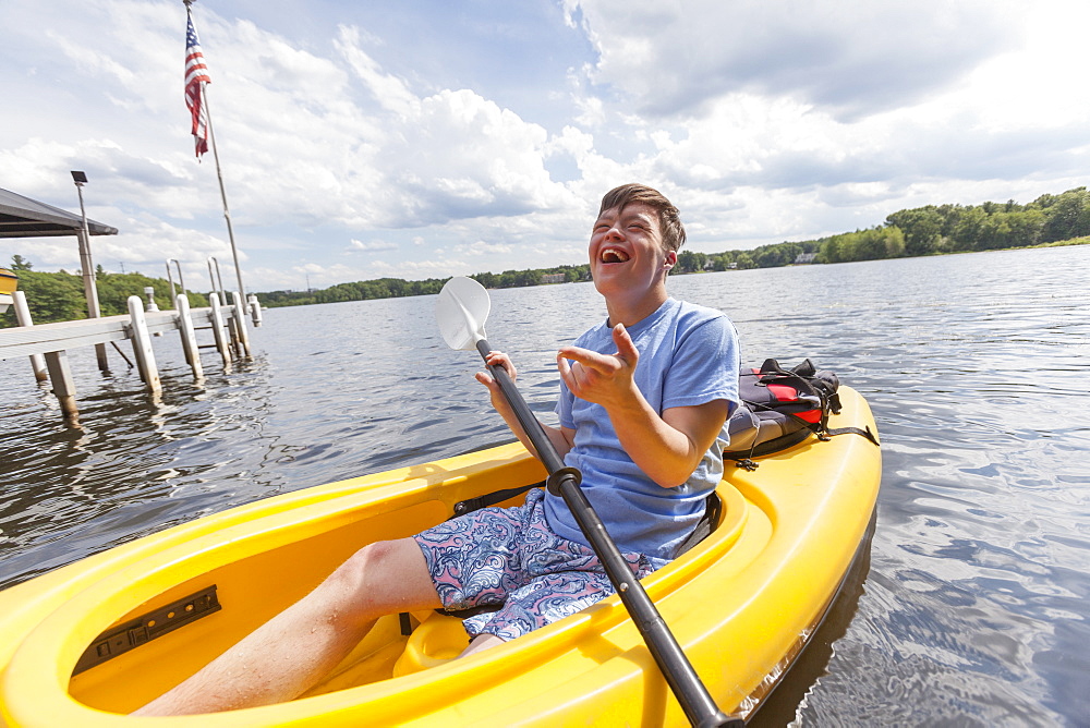 Happy young man with Down Syndrome rowing a kayak in a lake