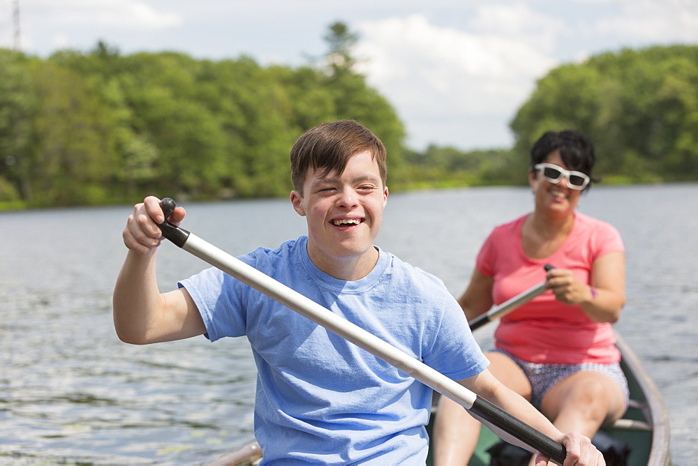 Young man with Down Syndrome rowing a canoe with his friend in a lake