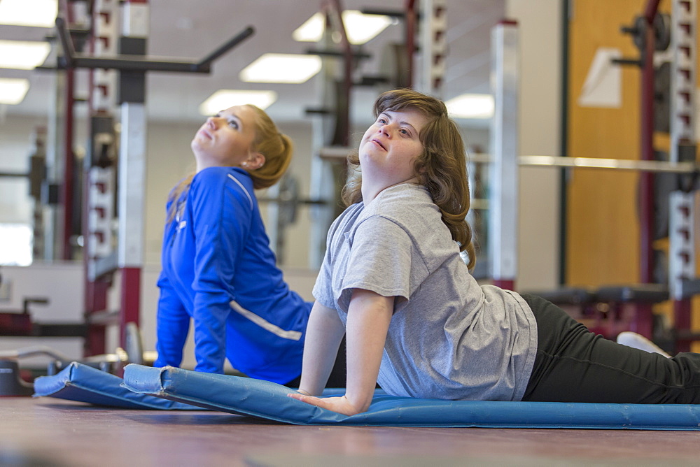 Young woman with Down Syndrome working out with her trainer on a exercise mat in gym