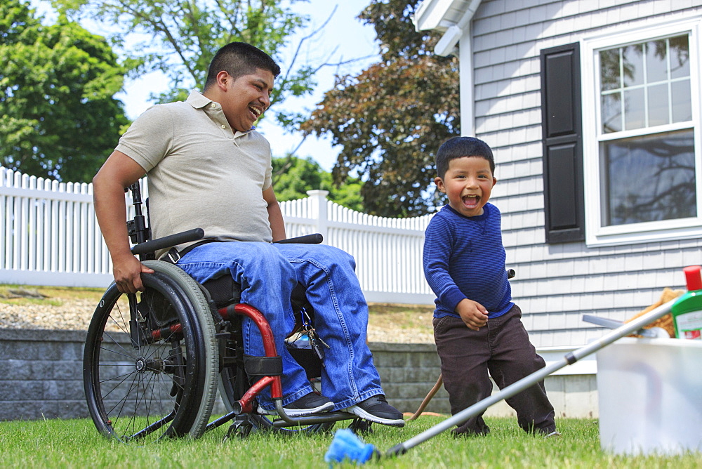 Hispanic man with Spinal Cord Injury in wheelchair with his son preparing to wash a car