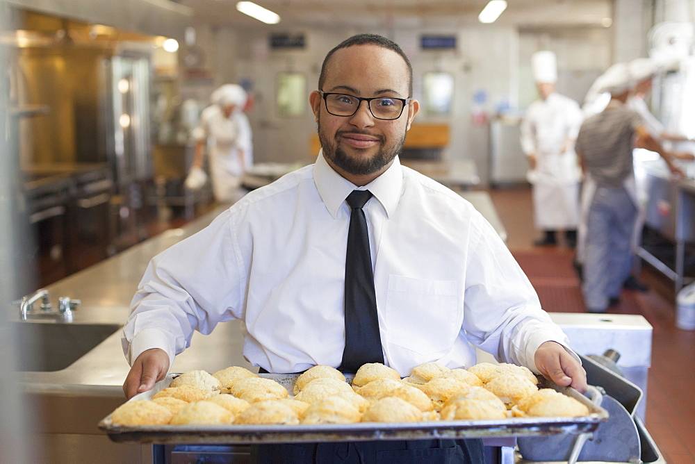 African American man with Down Syndrome as a chef holding a tray of cookies in commercial kitchen