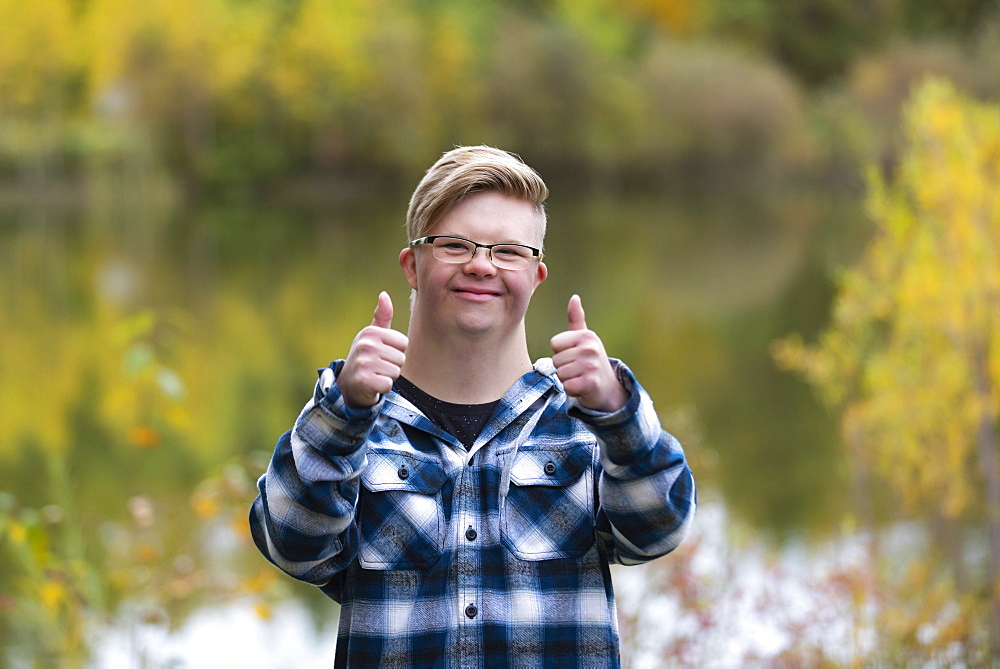 A young man with Down Syndrome giving a thumbs up in a city park on a warm fall evening: Edmonton, Alberta, Canada