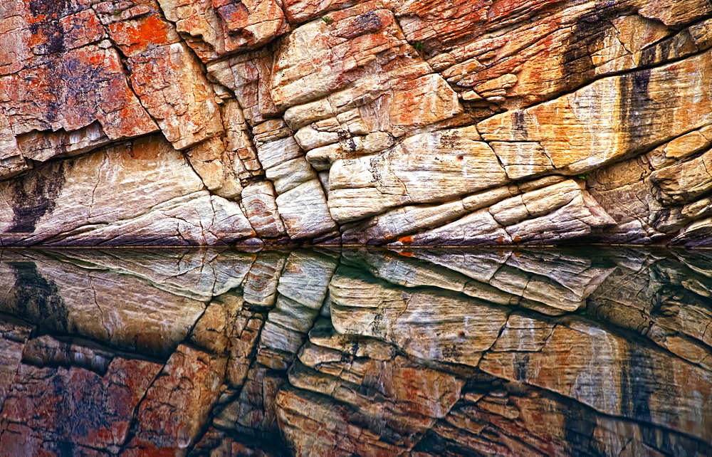 Rock wall surface reflected in tranquil water of Horseshoe Lake, Jasper National Park; Alberta, Canada