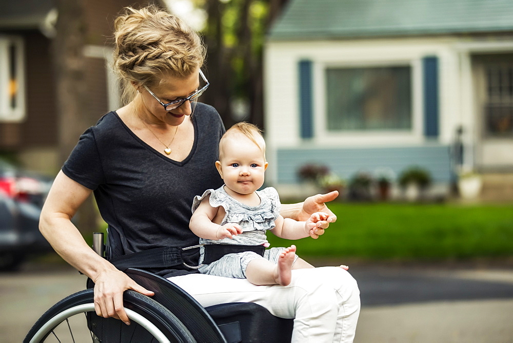 A paraplegic mom carrying her baby in her lap while using a wheelchair outdoors on a warm summer afternoon: Edmonton, Alberta, Canada