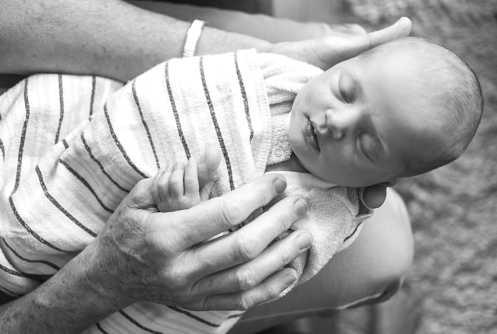 Newborn baby girl wrapped in a blanket and sleeping on her father's lap; Vancouver, British Columbia, Canada