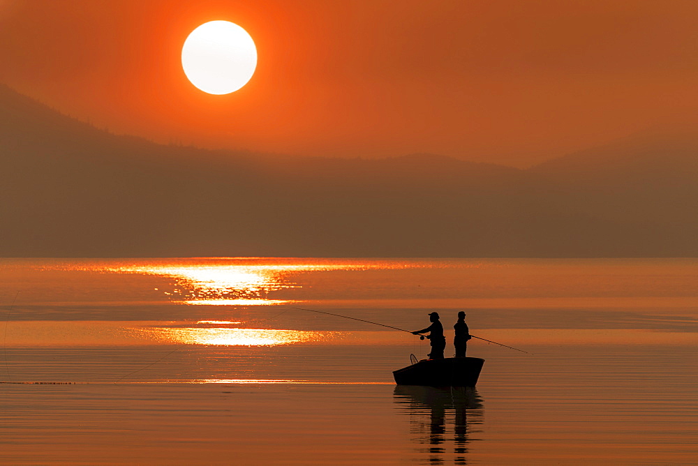 Silhouetted anglers standing in a boat fishing for salmon at sunset; Juneau, Alaska, United States of America