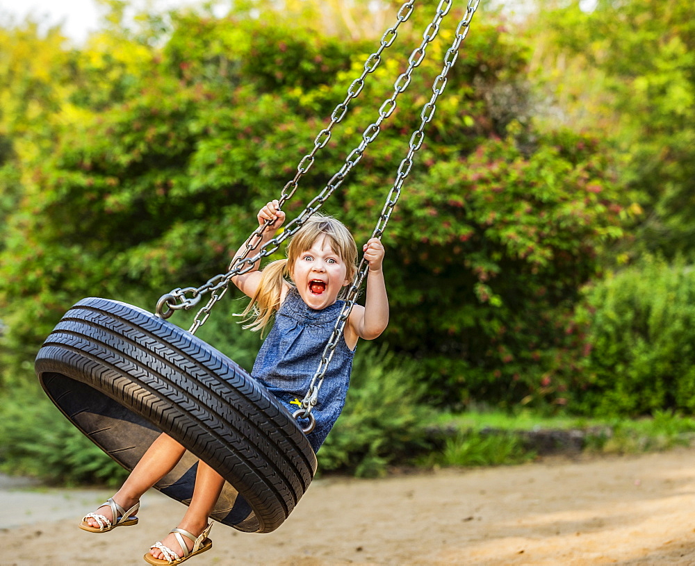 A young girl makes a silly face as she swings on a tire swing; Edmonton, Alberta, Canada