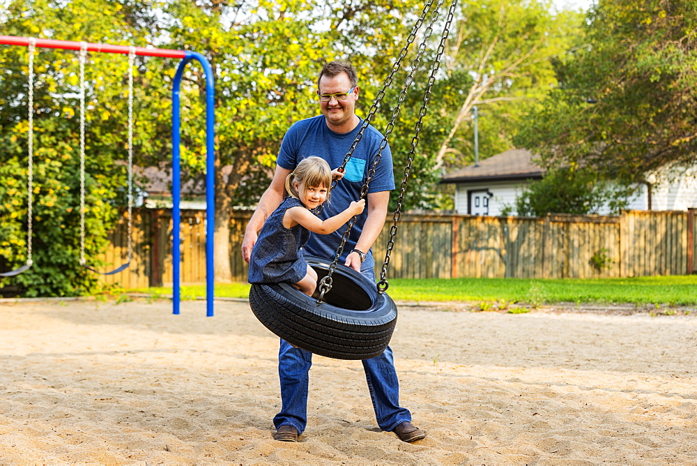 A father pushes his daughter on a tire swing at a playground; Edmonton, Alberta, Canada