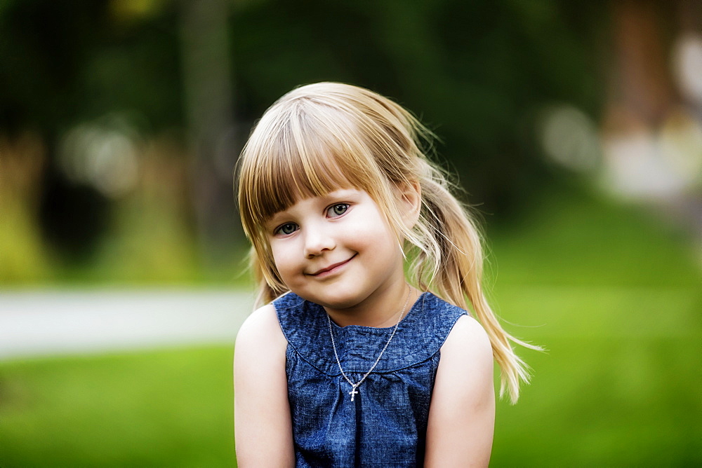 Portrait of a cute young girl with blond hair in pigtails and wearing a necklace with a cross pendant; Edmonton, Alberta, Canada