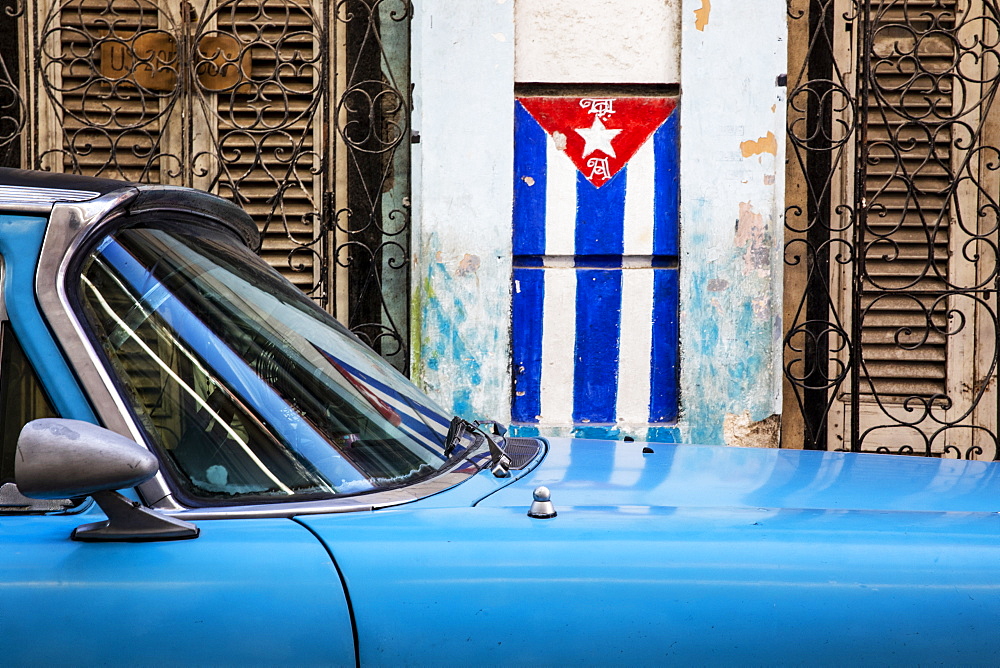 Cuban flag and blue car on the streets of Havana; Havana, Cuba