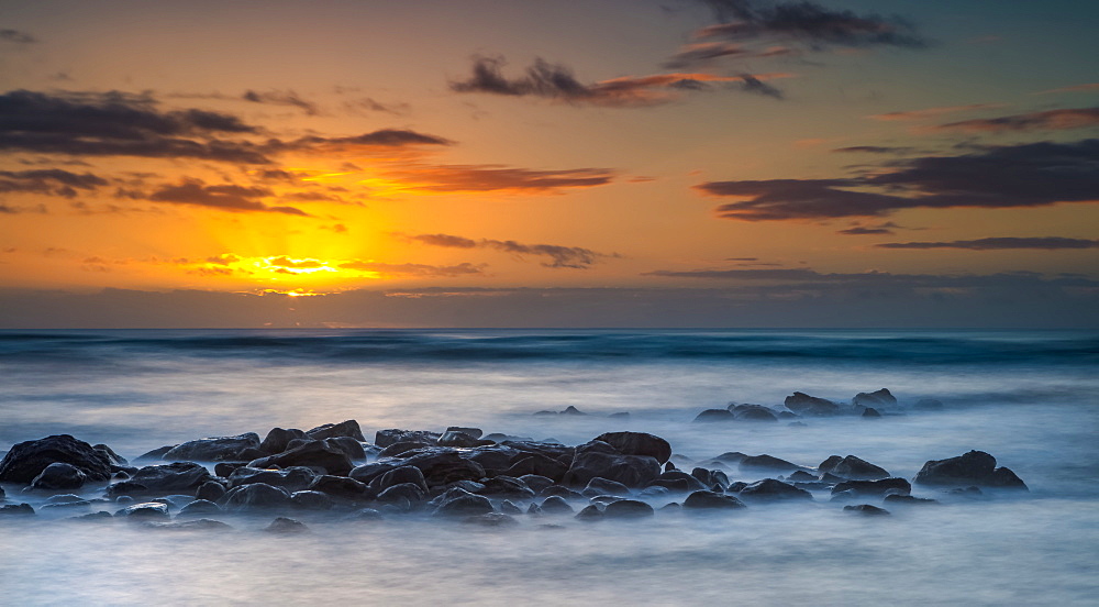 Sunrise over the Pacific Ocean from the rocks on the shore of Kauai; Kauai, Hawaii, United States of America