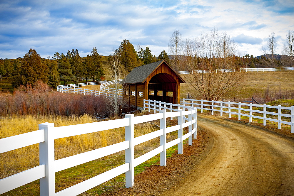 Covered bridge over a river in the countryside with dirt road; Oregon, United States of America