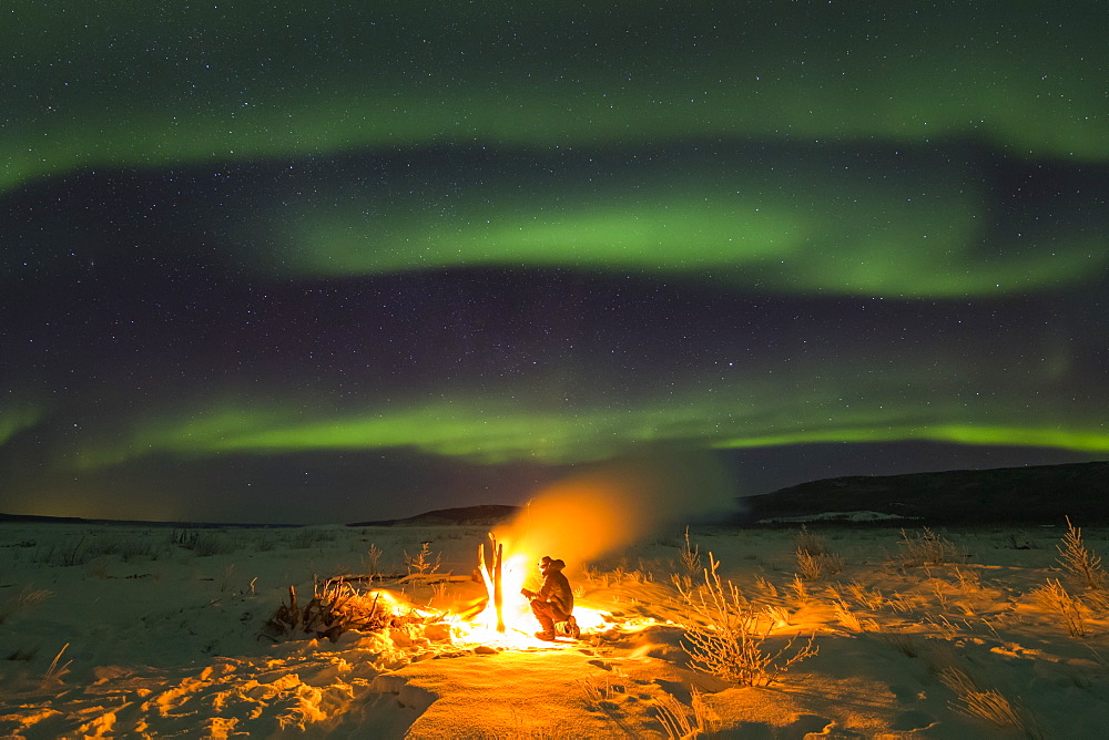 Staying warm beside a campfire on the Delta River while watching the aurora borealis on a frigid night; Alaska, United States of America