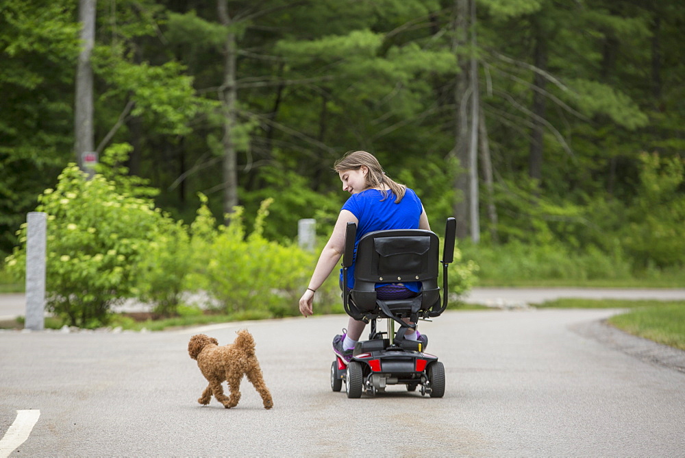 Young Woman with Cerebral Palsy playing with her dog while sitting on her scooter