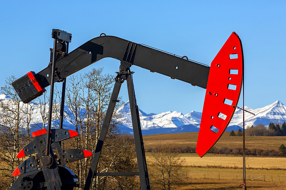 Pumpjack in a field with the foothills and snow-covered Rocky mountains in the background; Alberta, Canada