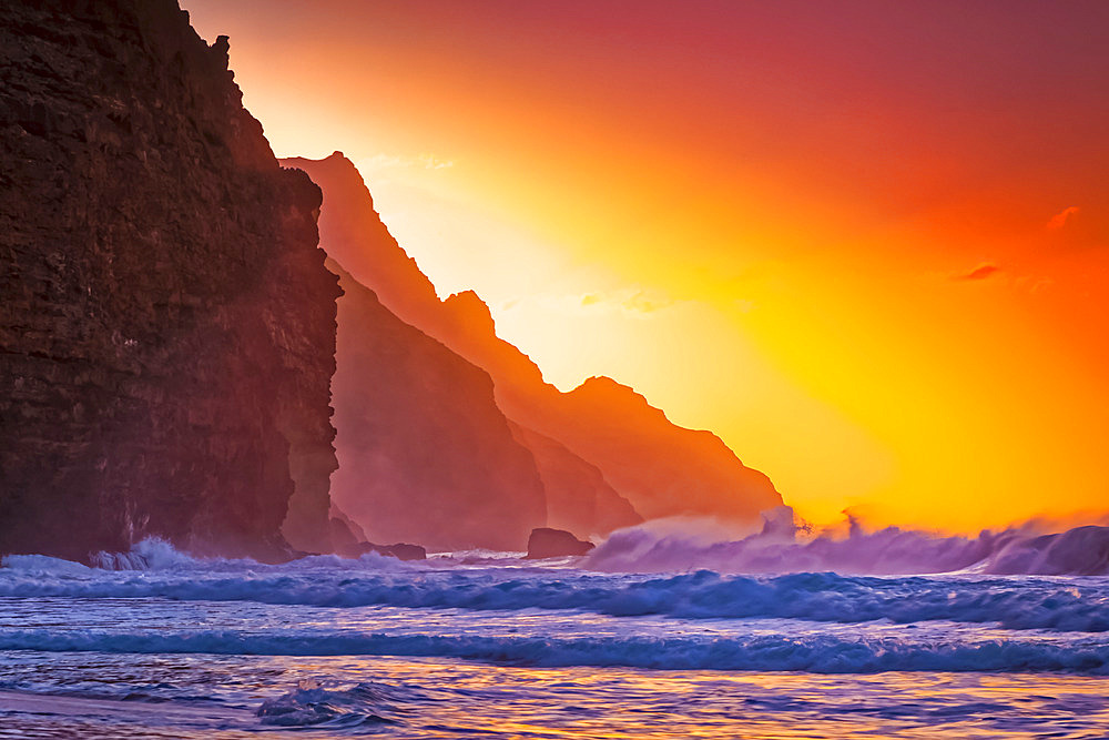 Bright orange sunset behind the rugged mountains along the Na Pali Coast, Kalalau Beach, Na Pali Coast State Park; Kauai, Hawaii, United States of America