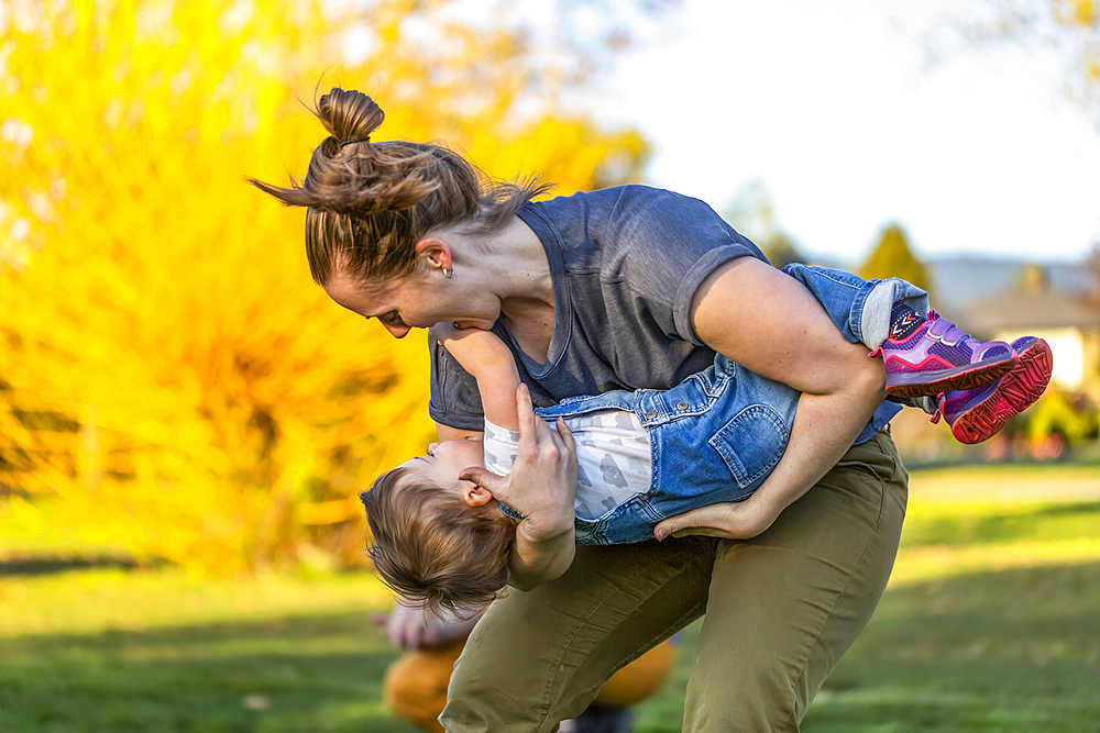 A mother plays with her toddler daughter in a park with autumn colours; North Vancouver, British Columbia, Canada