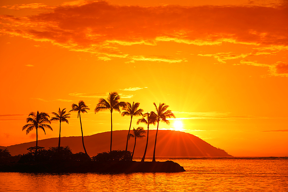 Sunrise at Kahala Beach, Waiʻalae Beach Park, with rays of the sun in a glowing sky reflected in the tranquil water; Oahu, Hawaii, United States of America