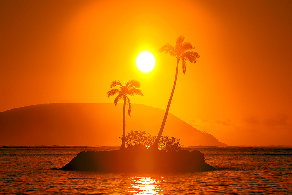 Sunrise at Kahala Beach, Waiʻalae Beach Park, with a flare around the sun in a glowing red sky reflected in the tranquil water; Oahu, Hawaii, United States of America