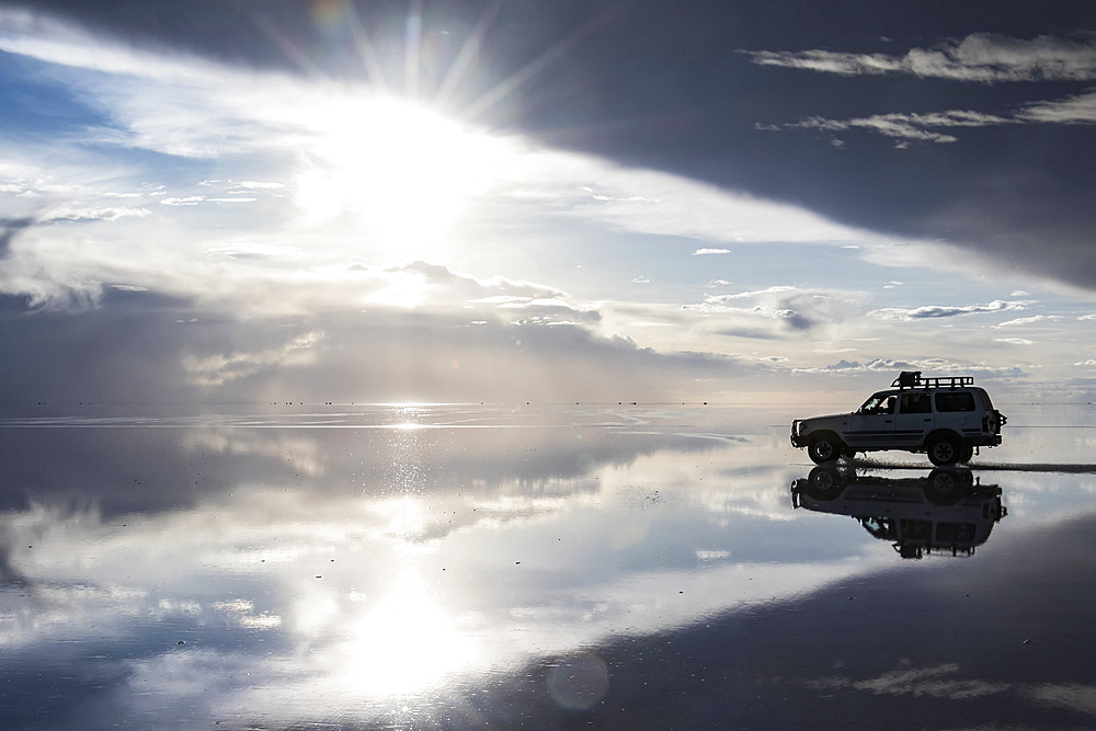 Four-wheel drive and reflection during the wet season (December-February) in Salar de Uyuni, the world's largest salt flat; Potosi Department, Bolivia