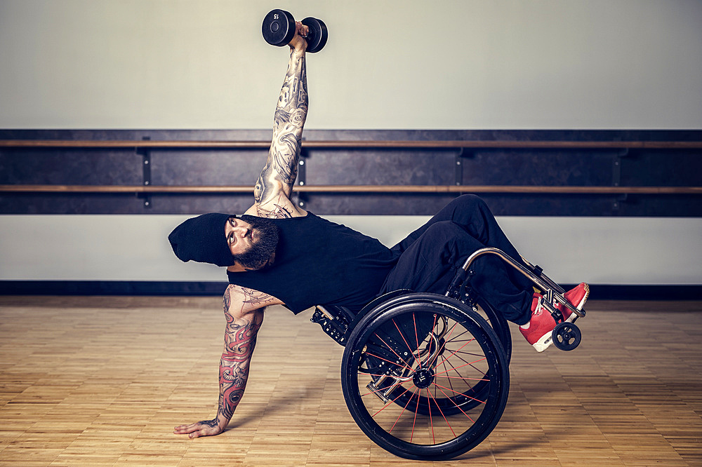 A paraplegic man popping a wheelie in his wheelchair and balancing while lifting a weight in a gymnasium after working out at a fitness facility: Sherwood Park, Alberta, Canada