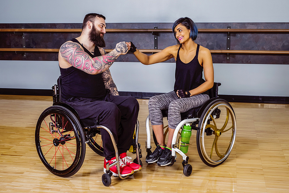 Two paraplegic friends giving each other a fist bump of encouragement after working out at a fitness facility: Sherwood Park, Alberta, Canada