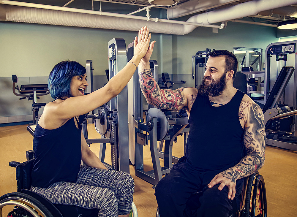 Two paraplegic friends giving each other a high five after working out at a fitness facility: Sherwood Park, Alberta, Canada