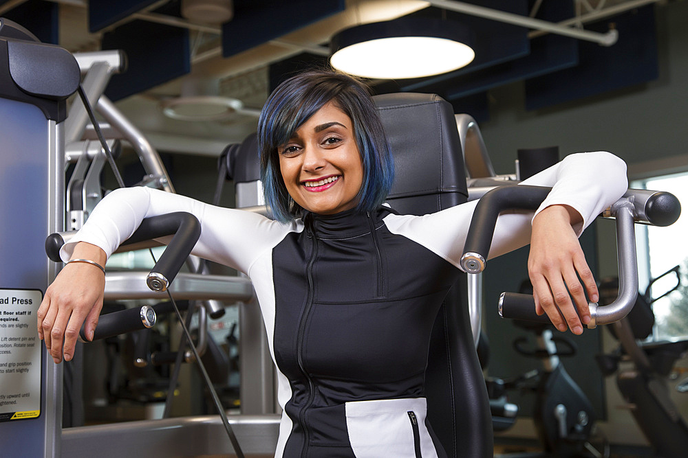 A paraplegic woman posing for the camera after working out using an overhead press in a fitness facility; Sherwood Park, Alberta, Canada