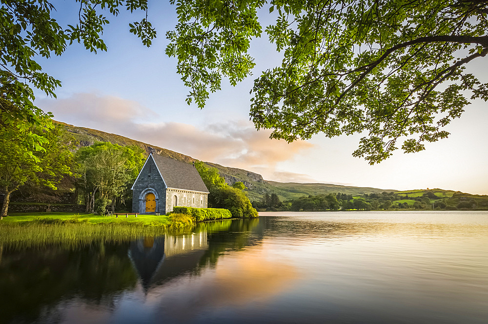 Old chapel of Gougane Barra situated by a lake and framed by green trees at sunrise; Gougane Barra, County Cork, Ireland