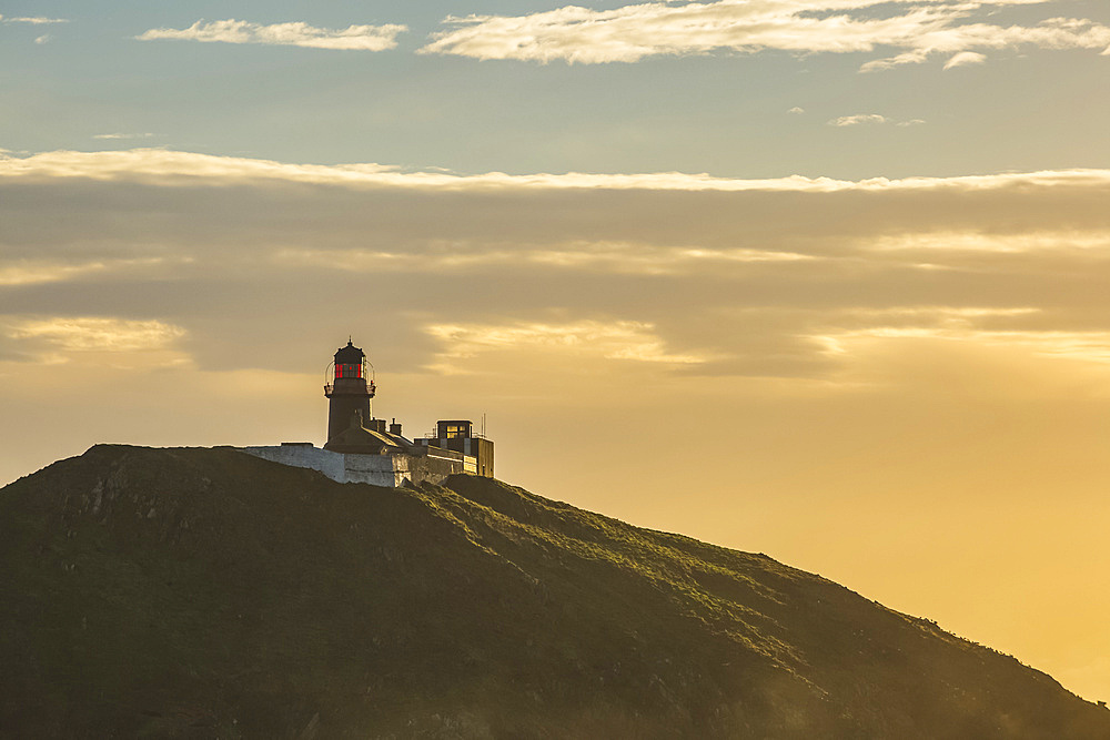 Silhouette of Ballycotton lighthouse being hit with the morning sun; Ballycotton, County Cork, Ireland