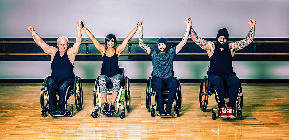 A group of paraplegic friends raising their hands together in victory after a workout in fitness facility: Sherwood Park, Alberta, Canada