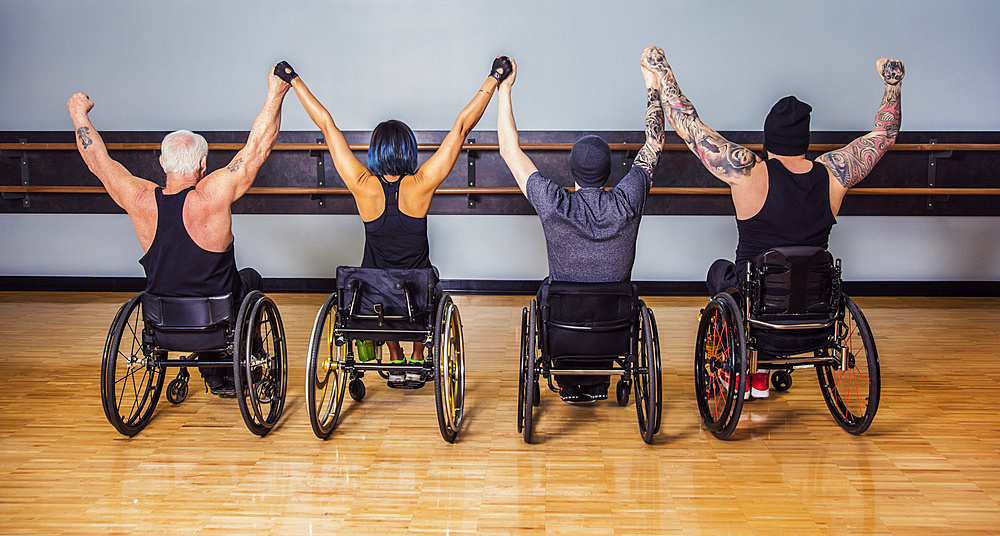 A view from behind of a group of paraplegic friends holding their hands high in a victory celebration after a workout in fitness facility: Sherwood Park, Alberta, Canada