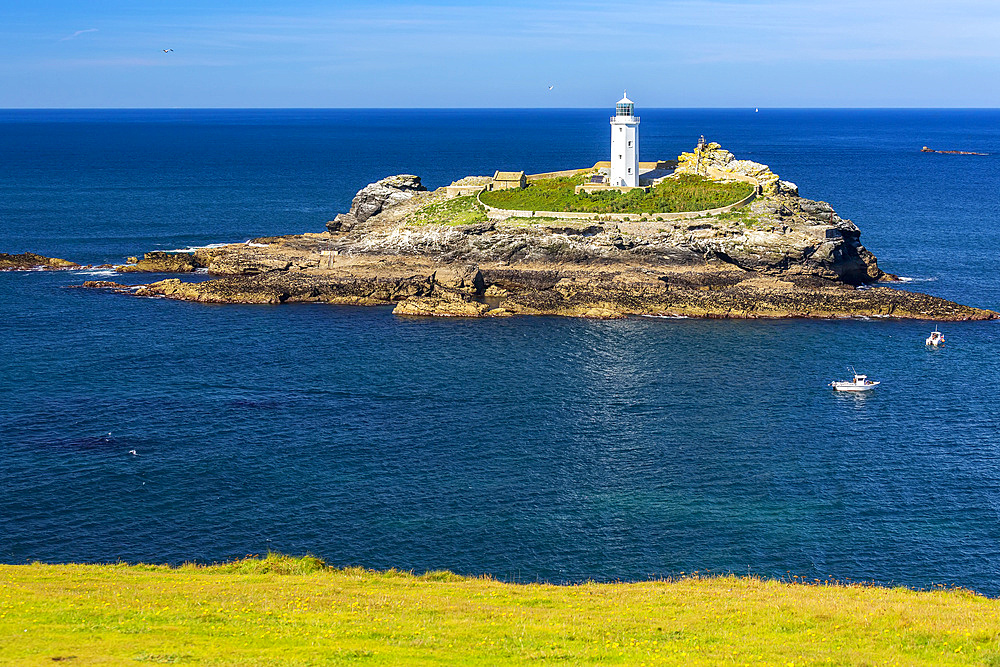 White Godrevy Lighthouse on rock formation in blue water with blue sky, Godrevy Island in St. Ives Bay; Cornwall County, England