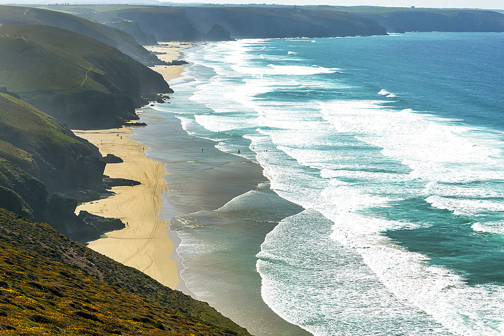 Sandy beaches with surf along a grassy cliff shoreline with blue sky and clouds; Cornwall County, England