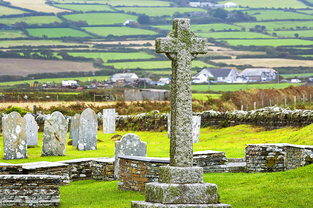 Old stone cross gravestone in graveyard with patchwork of fields in the background; Cornwall County, England