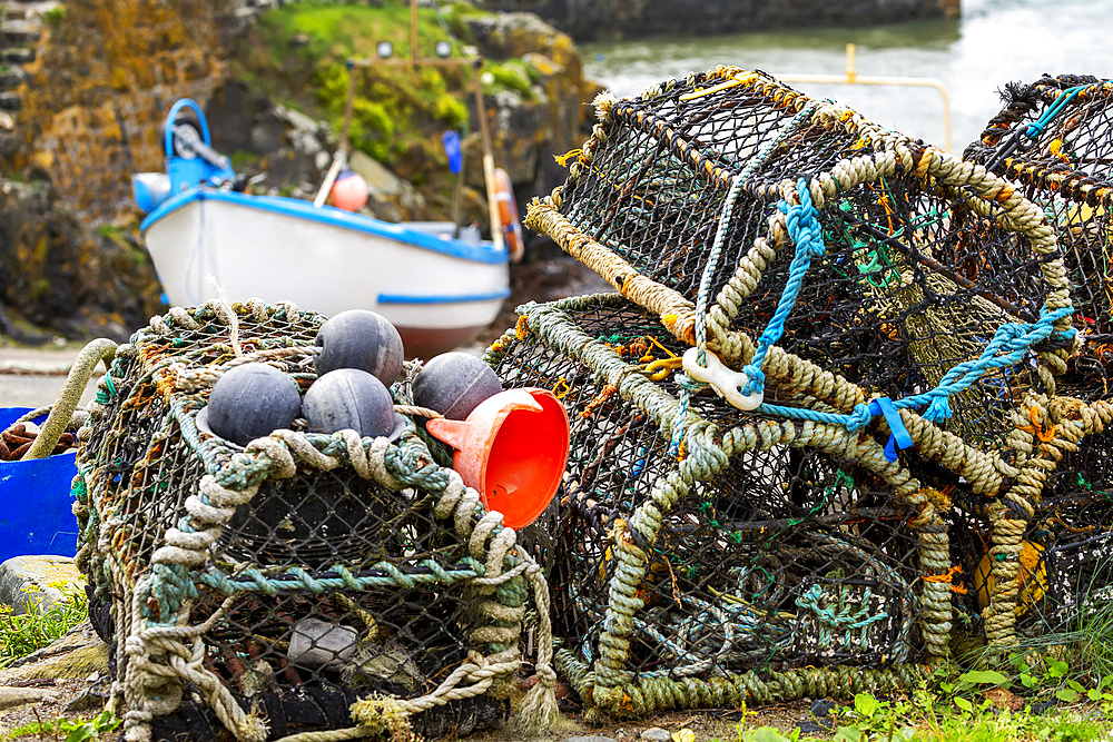 Close-up of lobster and crab cages stacked up, with fishing boat in the background; Cornwall County, England