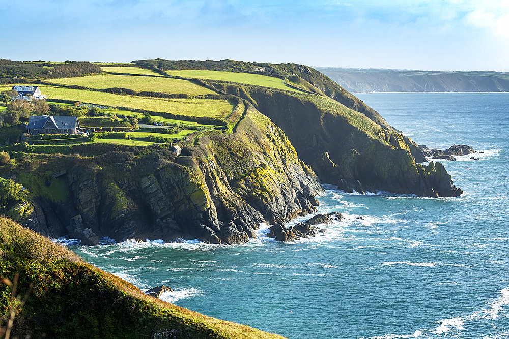 Rocky cliff shoreline with patchwork green fields and blue sky; Cornwall County, England