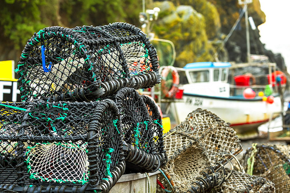 Close-up of lobster and crab cages stacked up, with fishing boat in the background; Cornwall County, England