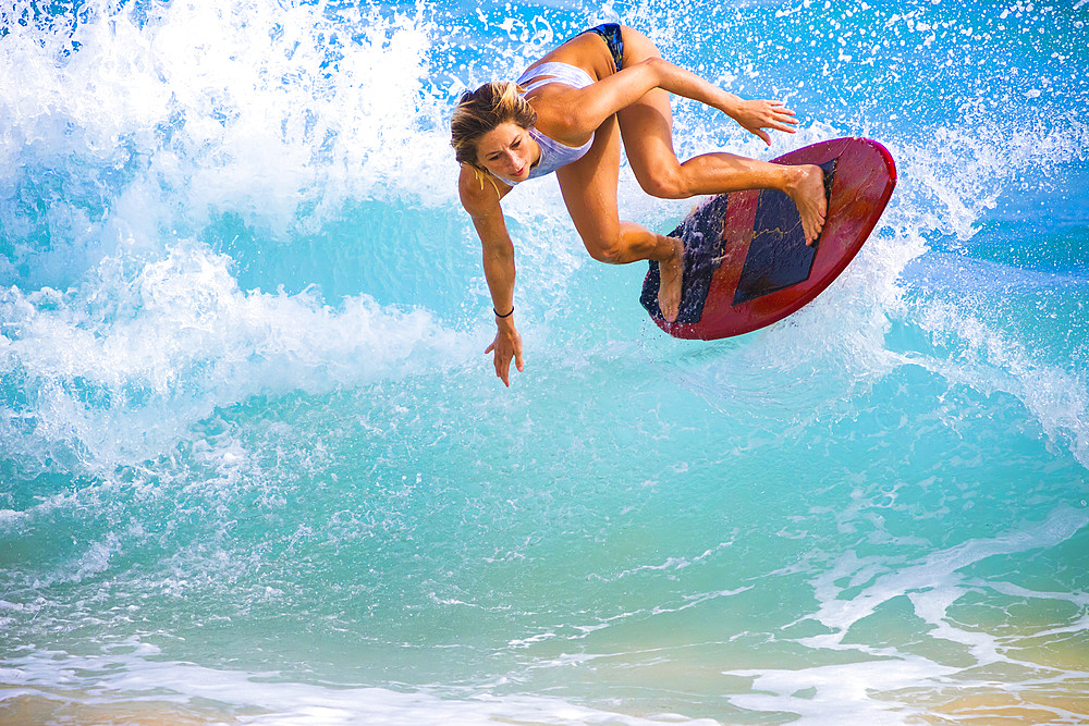 A young woman leaps in the air on a skimboard off Sandy Beach, Oahu; Oahu, Hawaii, United States of America