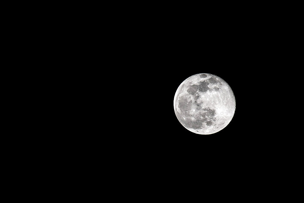 The snow moon as it was rising in the sky in the evening. Image was taken out on a frozen lake in Minnesota. Another name for this full moon is the starving moon; Minnesota, United States of America