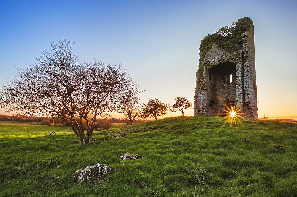 Old Irish castle ruins in a green field with the setting sun coming through the window hole; Clonlarra, County Clare, Ireland