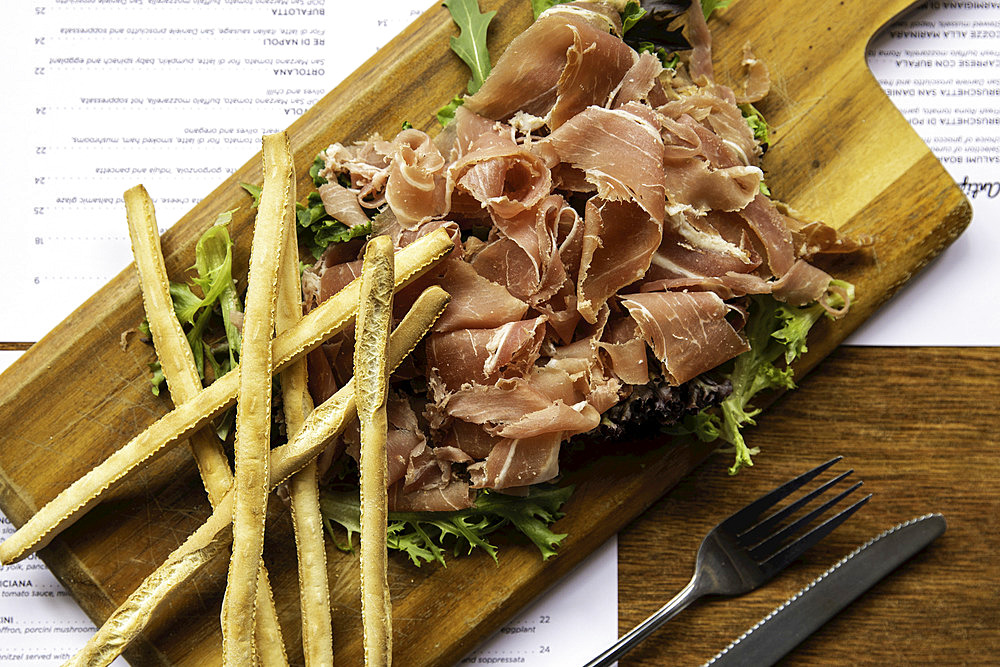 Prosciutto and grissini on wooden board; Melbourne, Victoria, Australia