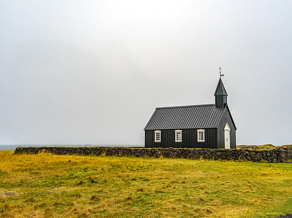 Church building with steeple and cross in a remote area with stone wall and grass; Snaefellsbaer, Western Region, Iceland